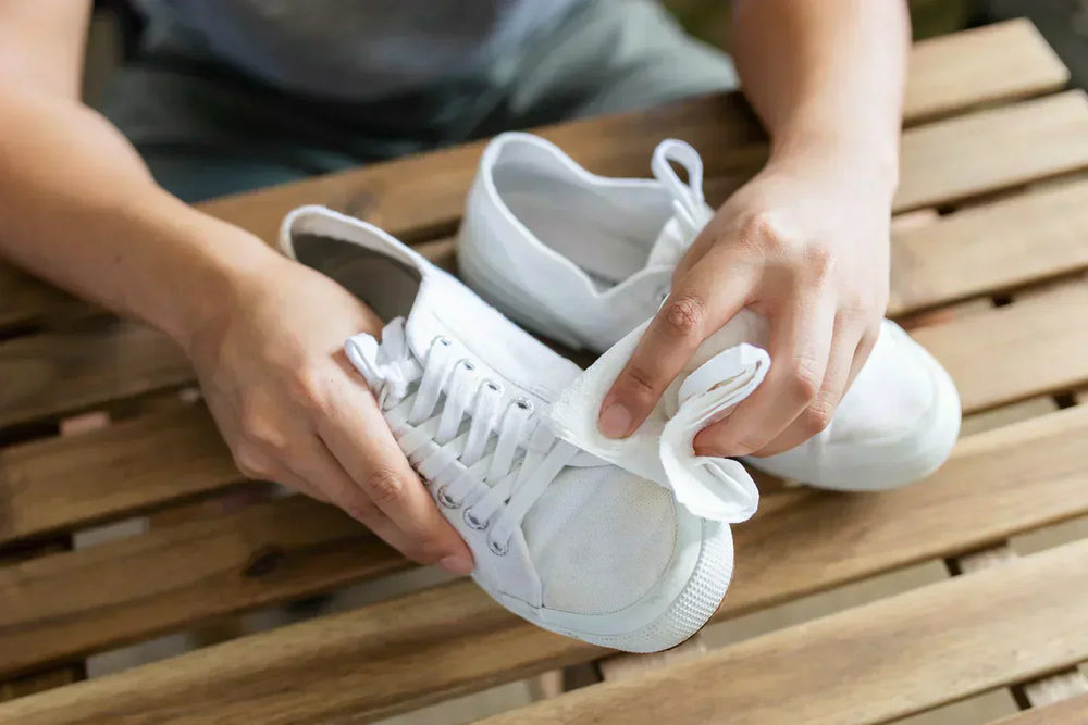 Person using a cloth to clean white canvas shoes with canvas shoe cleaning tips
