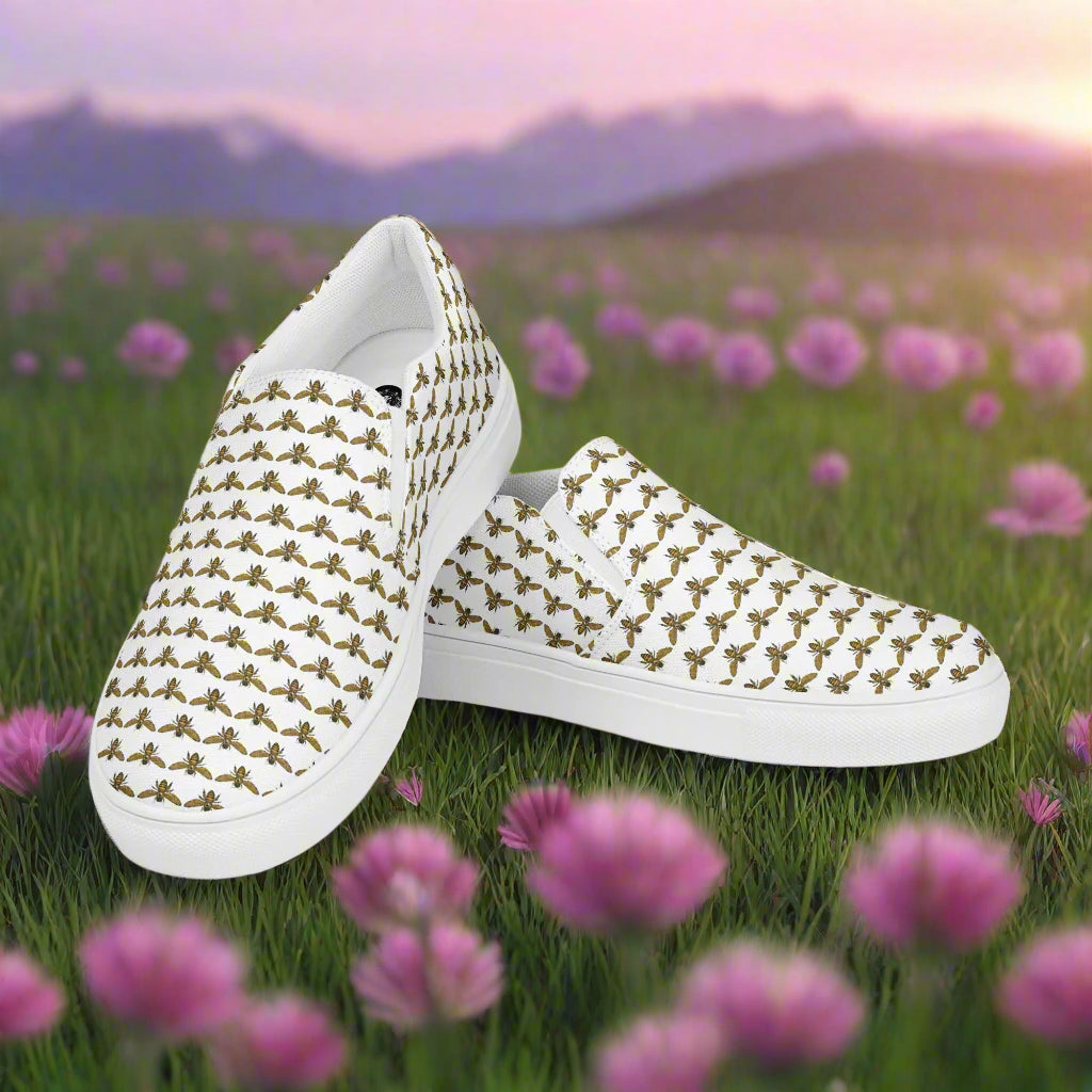 WildSage Market white bee pattern slip on shoes with repeated bee design on grass with flowers background