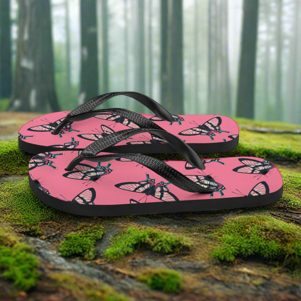WildSage Market butterfly print flip-flops in pink with black straps, set in a natural outdoors background