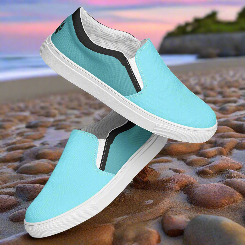 WildSage Market teal slip on canvas shoes with white soles on a rocky beach background