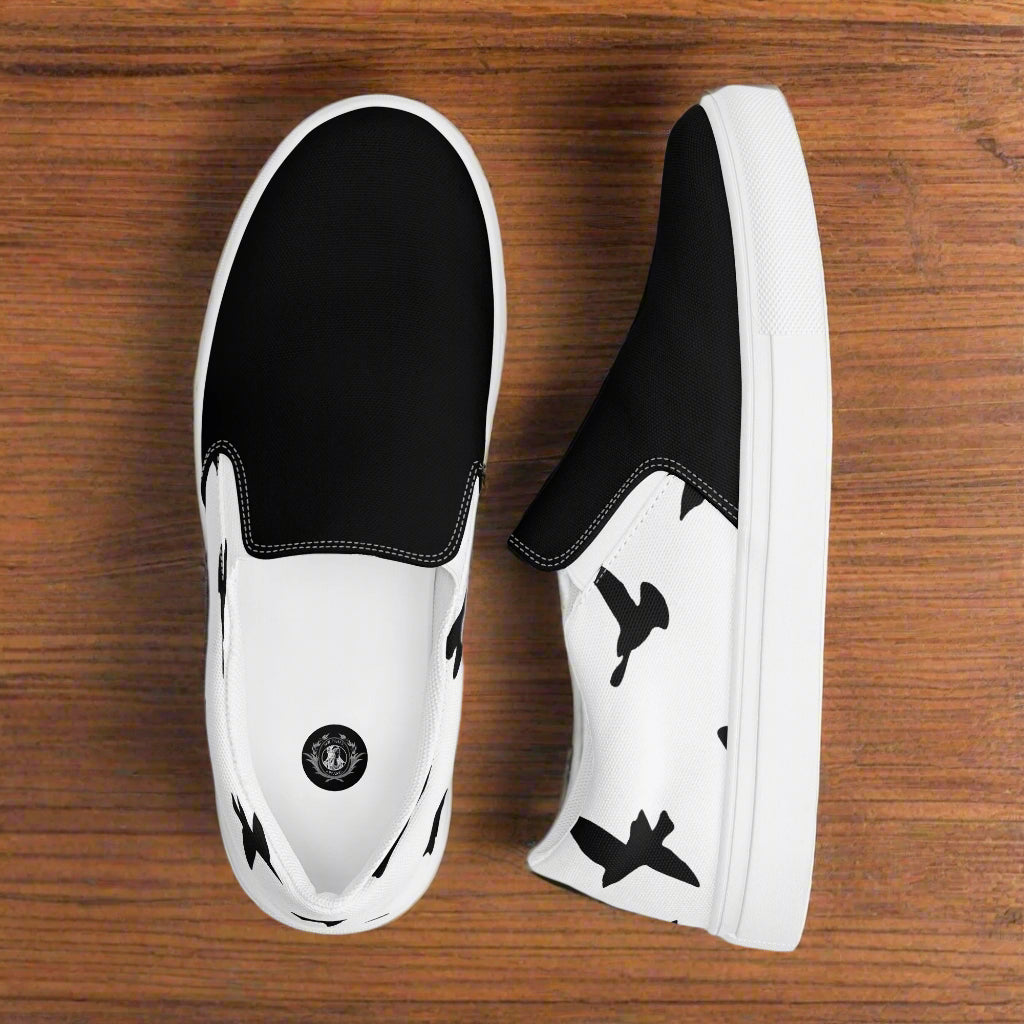 WildSage Market black and white Slip-on Canvas Shoes with bird print sides and white rubber sole on wood floor