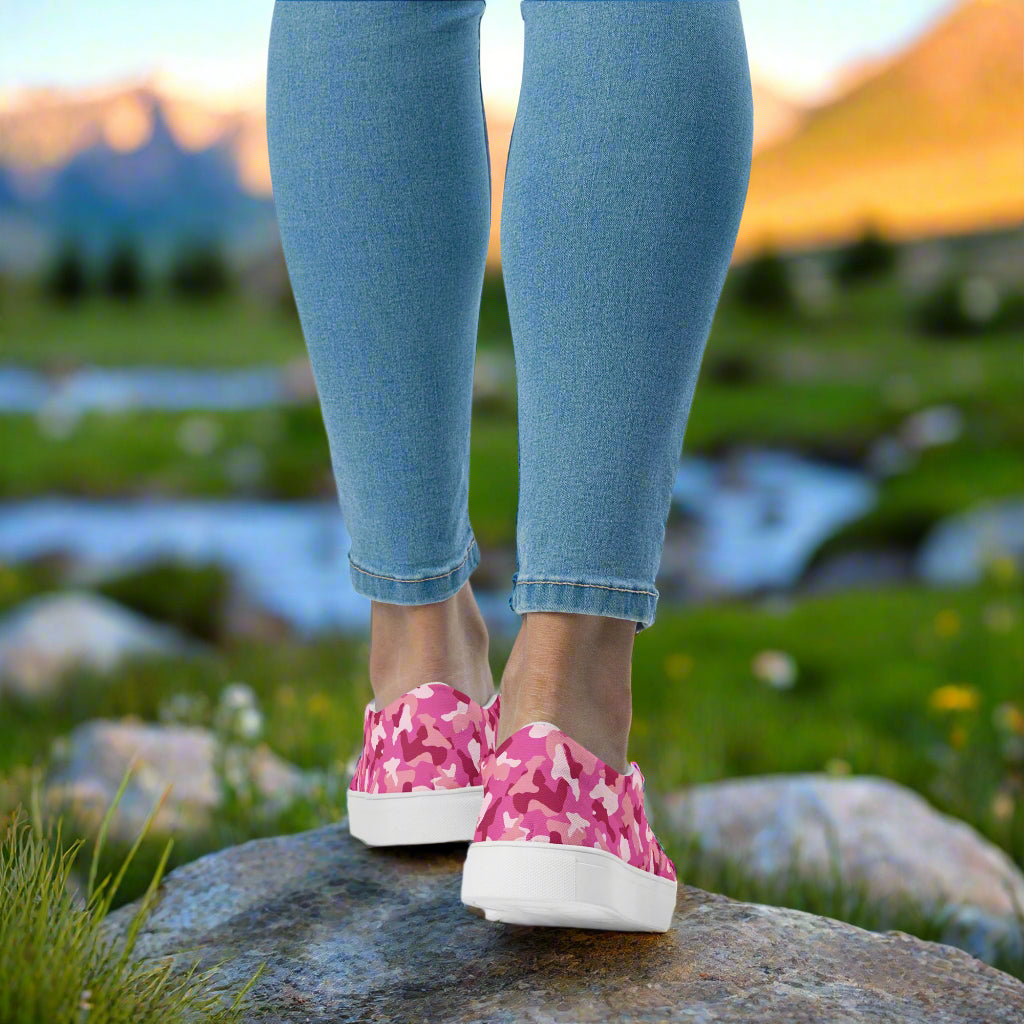 WildSage Market pink camo slip on shoes worn with jeans standing on a rock outdoors