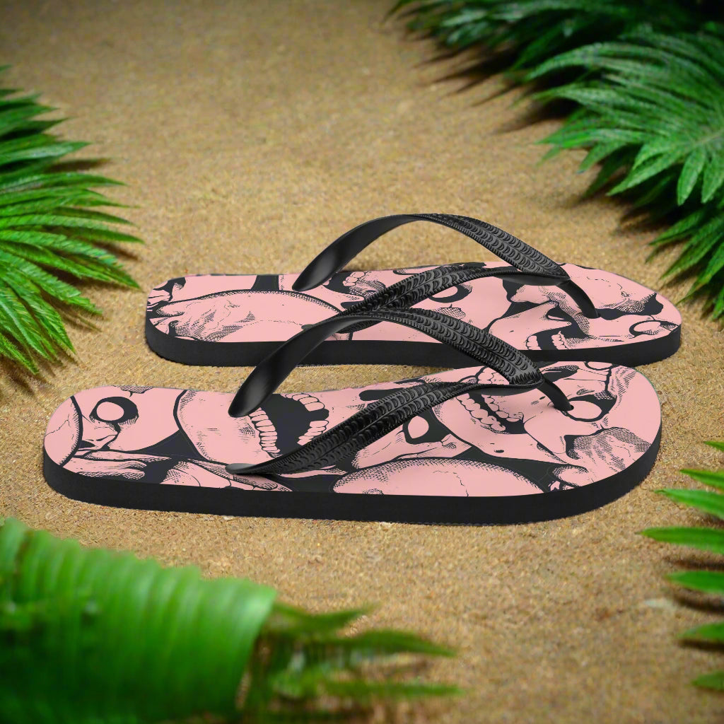 WildSage Market pink skull print flip flops on sandy beach with tropical foliage