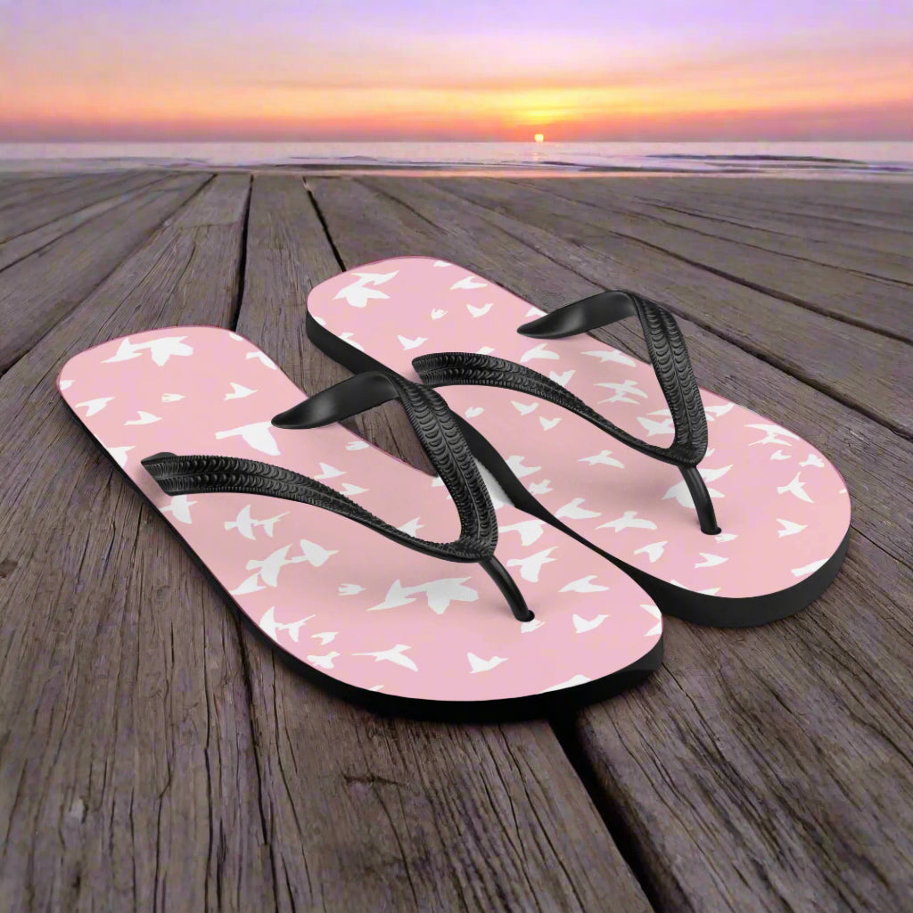 Pink White bird print flip-flops with black straps on a sunset beach boardwalk