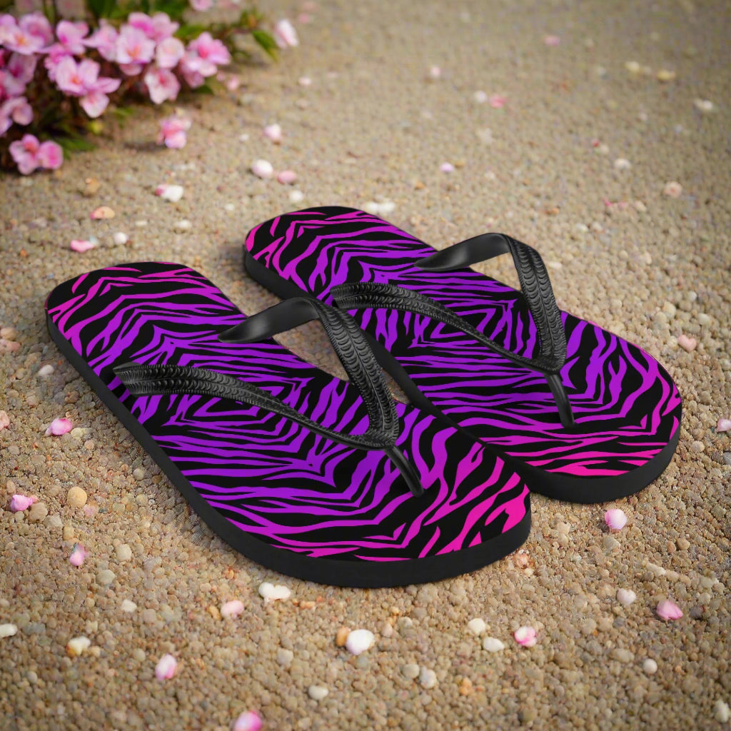 WildSage Market purple zebra print flip-flops with black straps on sandy background