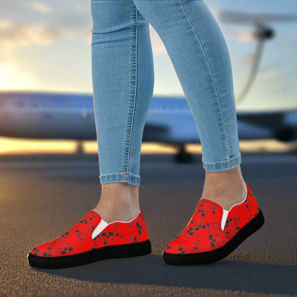 Skull Pile Red Slip-On Canvas Shoes on a person with denim jeans at an airport runway