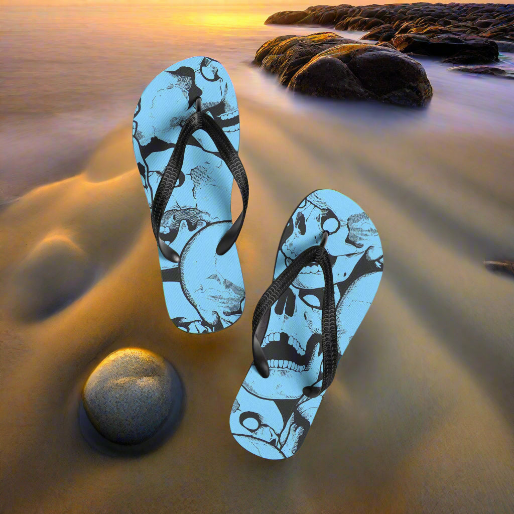 Skull Print Flip-Flops Light Blue with Black Straps on a Sandy Beach Background