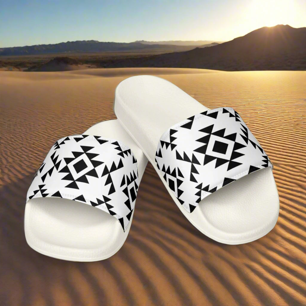 White slides with Southwest pattern in black geometric design displayed on desert sand at sunset