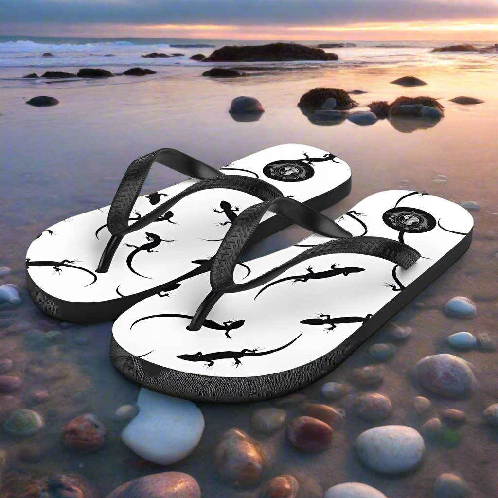 Stylish white lizard print flip-flops on a serene beach with stones and sunset backdrop