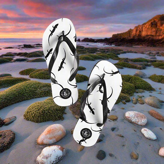 WildSage Market white lizard print flip-flops on a beach with a scenic sunset background