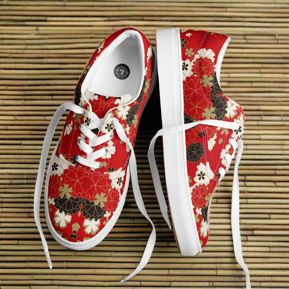 A pair of red custom low-top lace up canvas sneakers with intricate Japanese-inspired floral patterns in black, white, and gold, featuring chrysanthemum-like motifs, placed side by side on a textured tan bamboo mat against a neutral background.
