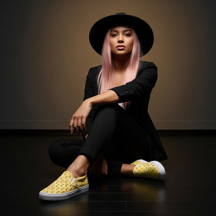 Stylish woman wearing casual yellow slip-on womens shoes with black outfit and hat sitting on dark floor