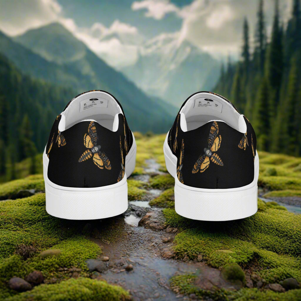 Black Moth Slip-on Canvas Shoes featuring a unique moth design on a scenic backdrop