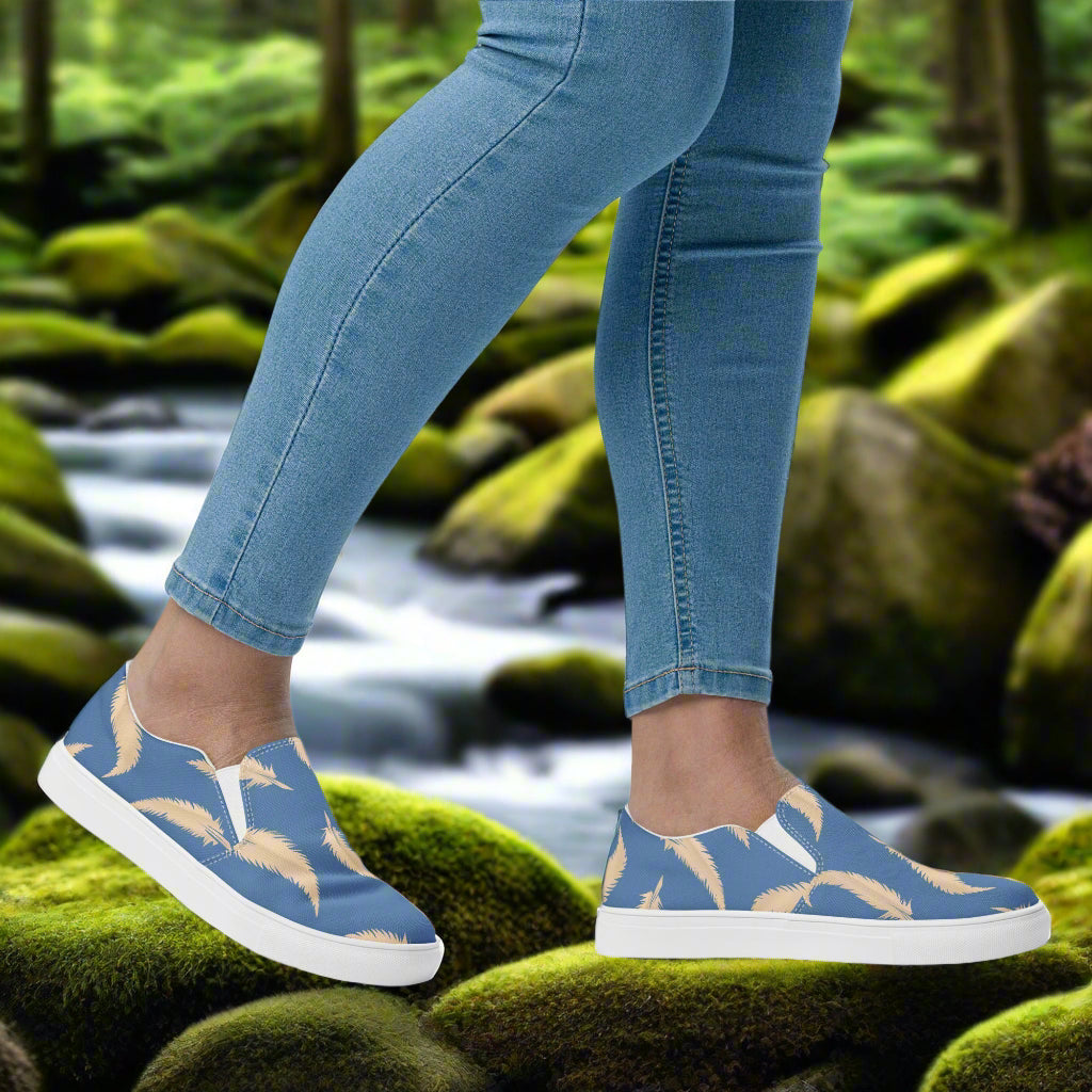 Blue Feather Slip-on Canvas Shoes displayed on a model's foot next to a serene natural backdrop
