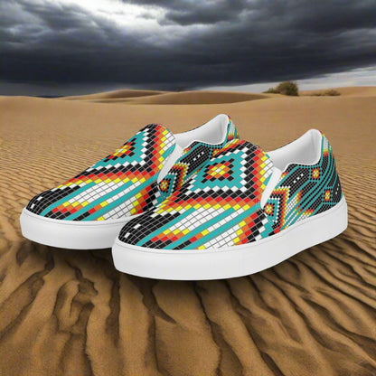 Mens Southwest canvas slip-on shoes with vibrant geometric pattern on a sandy desert backdrop.