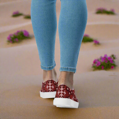 Woman wearing Slip-on Canvas Shoes Red Mesa Southwest Print with denim jeans, walking on a sandy path