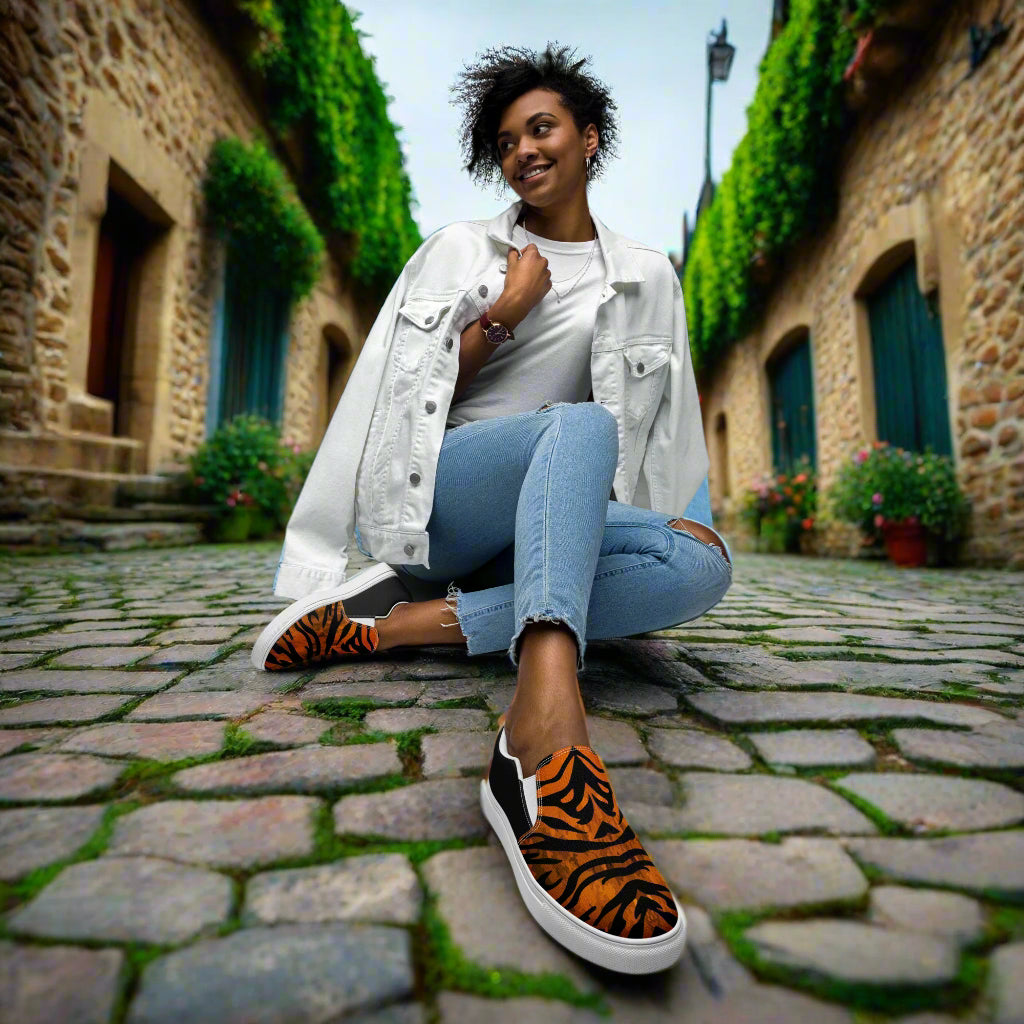 WildSage Market slip on shoes featuring tiger print halftone design worn by woman sitting on cobblestone street